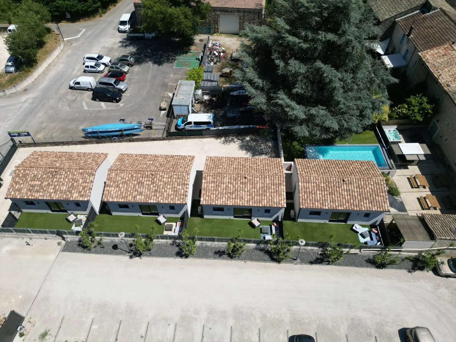 Vue aérienne verticale : les quatre gîtes alignés avec leurs jardinets, la piscine, le jacuzzi et la cuisine d’été sous un grand cèdre