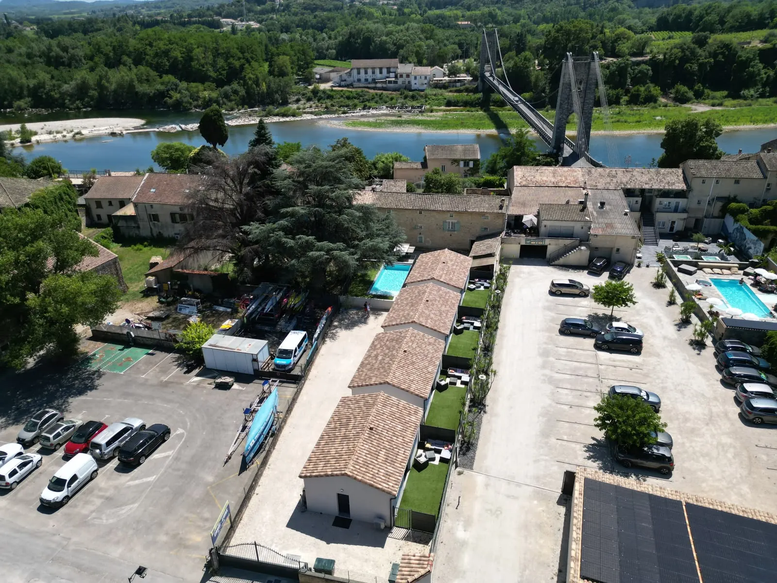 Vue aérienne : les quatre gîtes au premier plan, puis les toits du village, la rivière Ardèche et le pont suspendu
