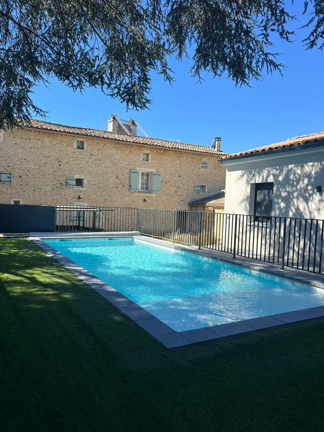Piscine commune entre une maison en pierre et le pignon d’un gîte